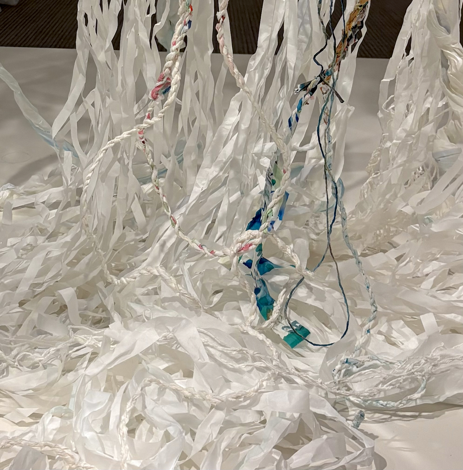 Paper strips and thread drape down and curl back on themselves. A few select areas are painted and stained with deep blue-greens, soft pinks, and yellow ochre.